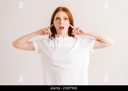 Ritratto della giovane donna stressata che copre le sue orecchie e gesticolante dire non bla-bla-bla in piedi su sfondo bianco isolato in studio. Foto Stock