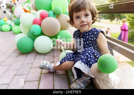 bambina con palloncini verdi in abito blu scuro Foto Stock