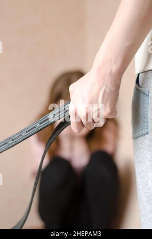 Violenza domestica contro i bambini. Mamma con una cintura si trova davanti al bambino. Figlia piangendo all'angolo Foto Stock