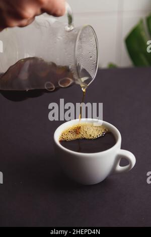 versare il caffè a mano dell'uomo dalla caffettiera in vetro in una tazza bianca. Foto Stock