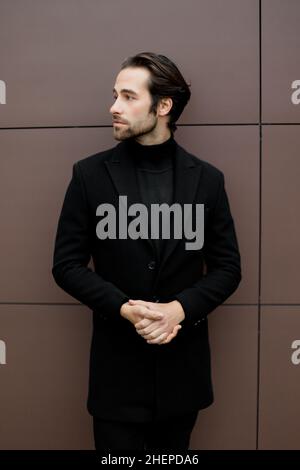 Uomo d'affari di successo in abito elegante e formale in piedi fuori dall'ufficio, guardando lateralmente, in posa per la fotografia. Bel maschio caucasico Foto Stock