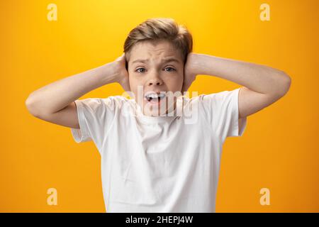 Il ragazzo emozionale sconvolto ricopre le orecchie con le mani su sfondo giallo Foto Stock