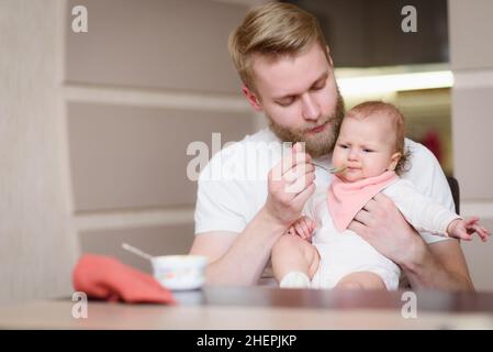 Papà nutre il suo bambino naughty che si rifiuta di mangiare purea di frutta Foto Stock