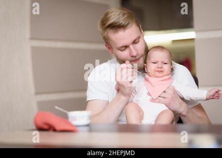 Il padre nutre la figlia naughty che rifiuta di mangiare gli alimenti complementari Foto Stock