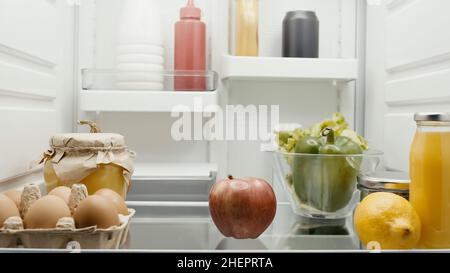 frutta fresca e verdure vicino alle uova, succo d'arancia e bottiglie con salse in frigorifero Foto Stock