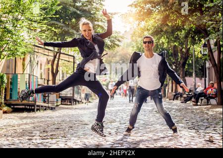 Donna attraente e bell'uomo con occhiali da sole che si divertono e saltano per strada. Stile di vita di moda Foto Stock