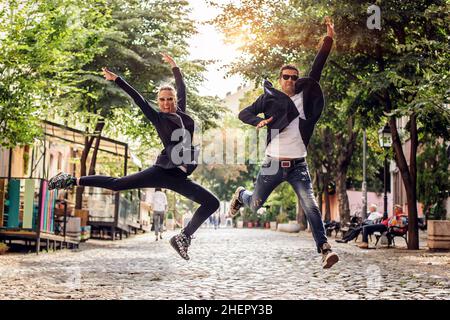 Donna attraente e bell'uomo con occhiali da sole che si divertono e saltano per strada. Stile di vita di moda Foto Stock