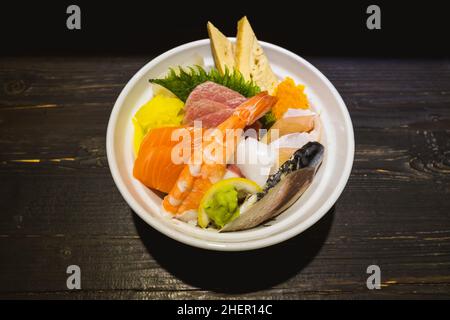 Vista dall'alto di Sashimi Don, Danburi o ciotola di riso giapponese con varie fette di pesce fresco, gamberi, calamari e uova di tamago, sul banco scuro in legno. Foto Stock