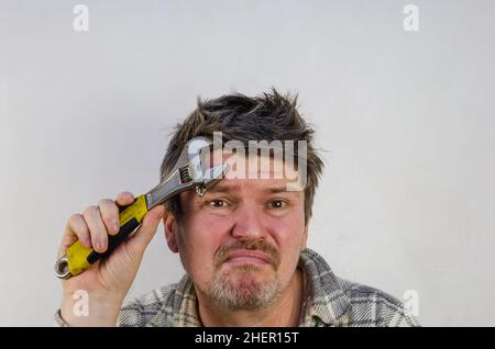 Un uomo adulto con capelli disevocati e aggrovigliati mette una chiave sulla fronte. L'uomo sta sperimentando un mal di testa. All'interno. Messa a fuoco selettiva. Foto Stock