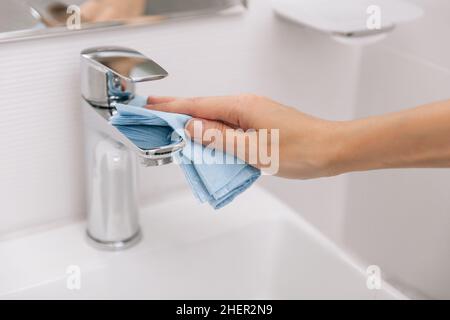 Pulire il rubinetto del lavello con un panno in microfibra. Pulizia del bagno. Igienizzare le superfici di prevenzione in ospedale e spazi pubblici contro corona Foto Stock