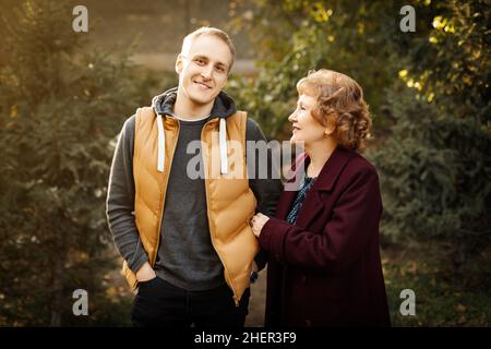 Mamma matura amorevole con il suo figlio adulto tra gli alberi autunno all'aperto. Foto Stock