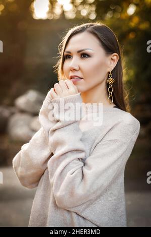Giovane donna carina in un maglione nella foresta autunnale tra gli alberi all'aperto. Foto di alta qualità Foto Stock