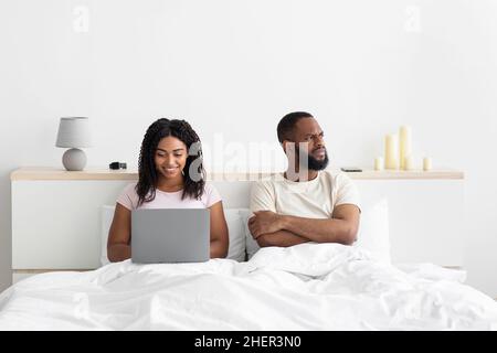 Offeso il triste giovane africano americano uomo con le braccia incrociate sul suo petto ignora la donna con il computer Foto Stock