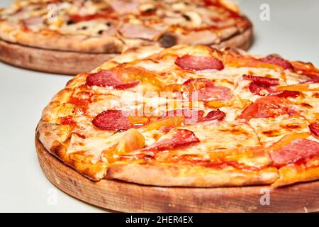 Pizza con salame, peperone, pomodori e formaggio su sfondo chiaro. Primo piano, messa a fuoco selettiva Foto Stock