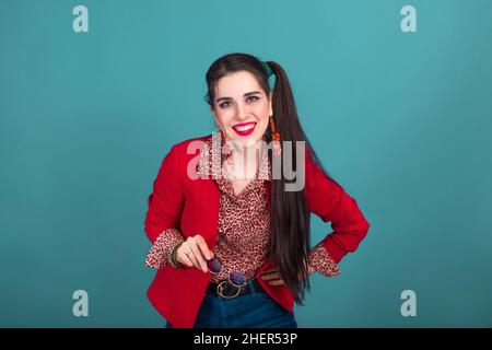 Giovane donna bruna sorridente in stile 90s in giacca rossa su sfondo blu. Foto Stock