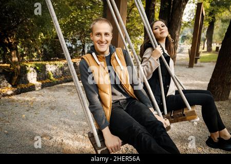 Felice coppia giovane su un dun altalena su un altalena in un parco forestale tra gli alberi in autunno. Foto di alta qualità Foto Stock