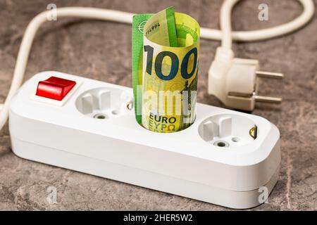 Banconota in euro inserita in una presa di prolunga. Aumento dei costi dell'elettricità per gli utenti aziendali e i clienti residenziali. Aumento dell'impianto elettrico Foto Stock