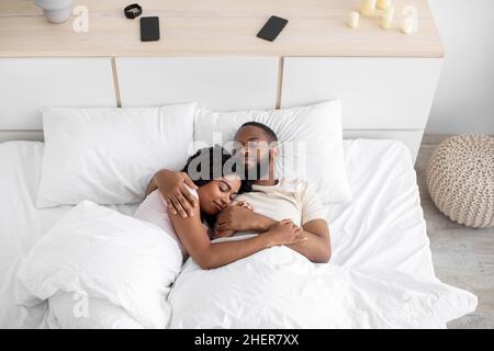 Amorevole felice uomo afroamericano millenario pacifico abbraccia la sua donna e dorme sul letto comodo insieme in camera da letto Foto Stock