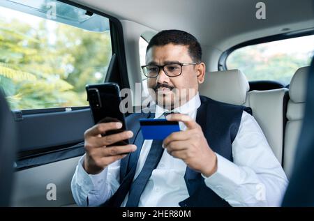 giovane uomo d'affari indiano shopping online o pagare fatture su telefonino utilizzando la carta di credito mentre si viaggia in taxi auto - concetto di pagamento digitale Foto Stock