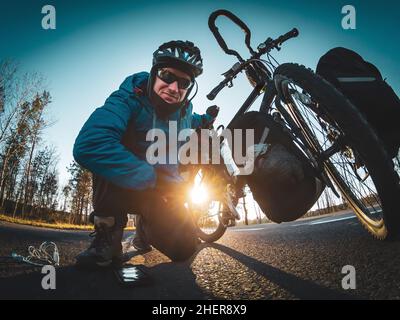 Il ciclista sul lato della strada sorrette le ginocchia in posa per l'Action Cam e tenendo la bicicletta con una mano e con gli accessori sul grou Foto Stock