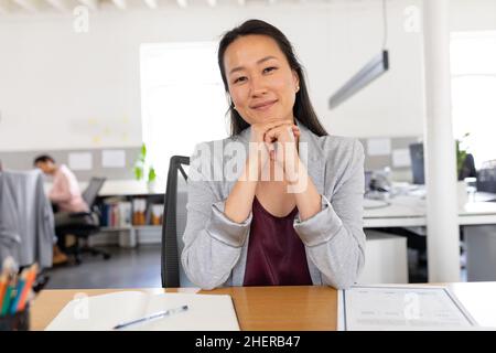 Ritratto di fiducioso asiatico creativa businesswoman seduta con mani sul mento alla scrivania in ufficio Foto Stock