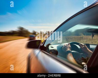 Il conducente di auto di fantasia sta tenendo il volante strettamente e cercando di passare un'altra auto di fronte durante la guida su strada grave in una campagna della Lettonia Foto Stock