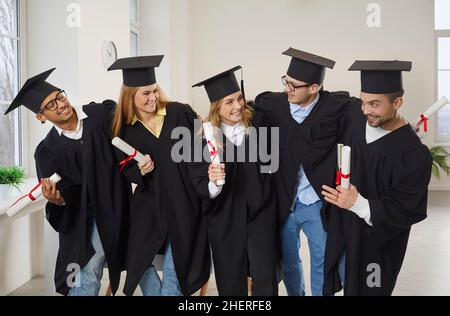 Un gruppo di amici universitari felici che si abbraccia in classe dopo la cerimonia di laurea Foto Stock