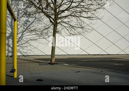 Un'altalena da gioco per bambini in un parco giochi. Un albero proietta ombre su un muro di casa. Foto Stock