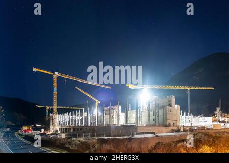 enorme cantiere di cemento di notte con quattro gru a torre stazionarie accanto all'autostrada Foto Stock