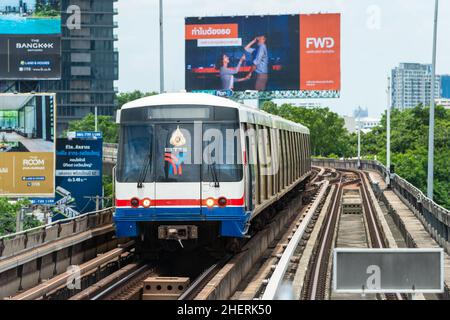 BTS Skytrain arrivo alla stazione Saphan Taksin di Bangkok. Grandi schede pubblicitarie sullo sfondo. Foto Stock