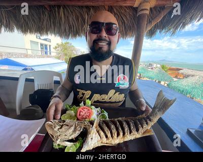 Erick Higuera o Pelon de Hospicio con un pesce curvina, branzino fritto in un ristorante di pesce e frutti di mare sulla spiaggia di Kino Bay, sonora. (Foto di Luis Gutierrez / NortePhoto) Erick Higuera o Pelon de Hospicio con un pescado curvina, corvina frita en restaurante de pescados y mariscos en la baia di playa Kino, sonora. (Foto di Luis Gutierrez / NortePhoto) Foto Stock