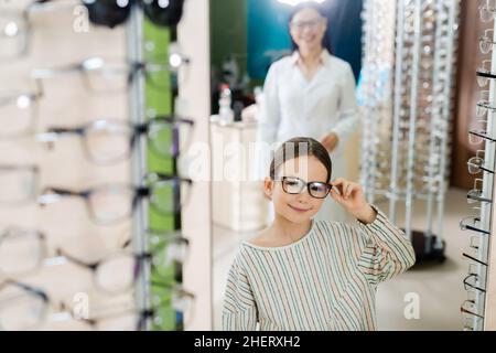 ragazza felice che regola gli occhiali vicino offuscato oftalmologo asiatico in negozio di ottica Foto Stock