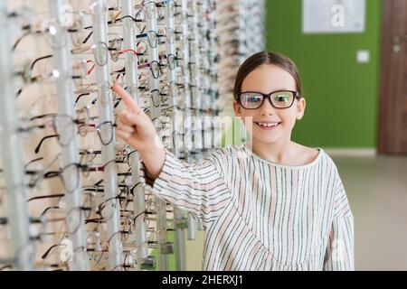 ragazza felice che punta con il dito mentre sceglie gli occhiali in negozio di ottica Foto Stock