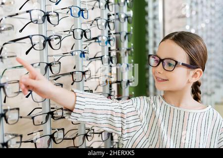 bambino positivo che punta all'assortimento di occhiali in negozio di ottica Foto Stock