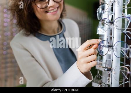 vista ritagliata della donna smiling blurred che sceglie gli occhiali in negozio di ottica Foto Stock