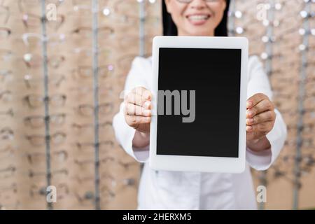 vista ritagliata dell'oculista sfocato che mostra un tablet digitale con schermo vuoto nel negozio di ottica Foto Stock