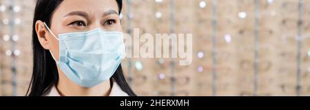 oftalmologo asiatico in maschera medica in salone di ottica su sfondo sfocato, banner Foto Stock
