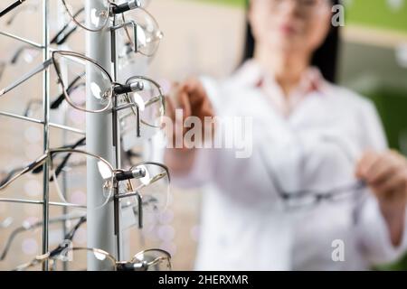 vista parziale dell'oculista sfocato che punta agli occhiali in un negozio di ottica Foto Stock