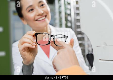 donna che punta con il dito agli occhiali in mano di felice oculista in negozio di ottica Foto Stock