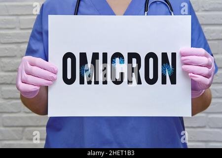 Una dottoressa tiene un foglio di carta con il testo della nuova variante del virus covid Omicron. Mani di un infermiere in guanti protettivi medici con un whit Foto Stock