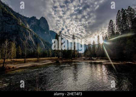 Alba con il sole che si staglia sul fiume e le montagne con le nuvole distintive come sfondo a Yosemite, California, Stati Uniti Foto Stock
