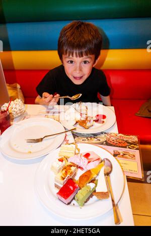 Giovane bambino caucasico, ragazzo, 8-9 anni, guardando lo spettatore mentre mangiano un piatto di torte al ristorante della catena giapponese 'paradiso dello zelo'. Foto Stock