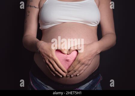 è un cuore rosa della ragazza con le mani sul ventre della madre incinta Foto Stock