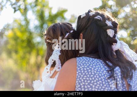 Vista posteriore di madre e figlia seduta in natura indossando belle trecce. Messa a fuoco soft Foto Stock