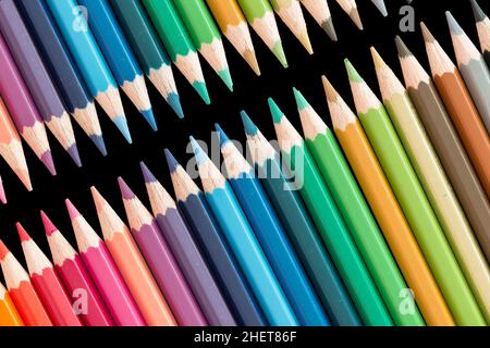 matite di legno di colore che giacciono in una fila su nero Foto Stock