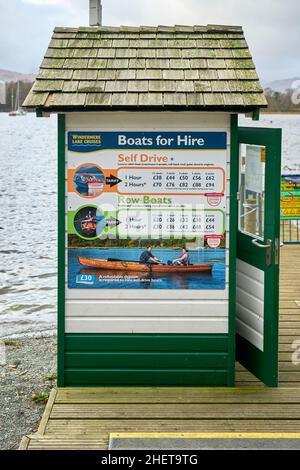 Biglietteria costruita in legno alla fine di un molo sul lago Windermere, Cumbria, Regno Unito, con tariffe di noleggio auto e barche a fila stampate su un cartello colorato Foto Stock