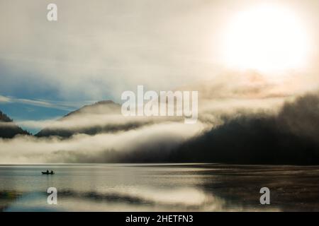 polvere mistica sul lago delle alpi austriache con barca pescatore e nebbia Foto Stock