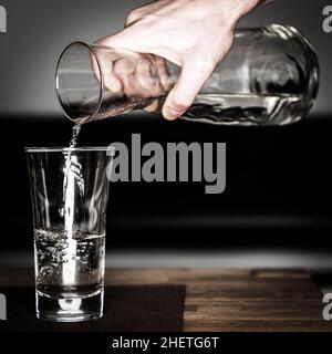 la mano si riempie d'acqua con una caraffa di vetro su un tavolo di legno Foto Stock