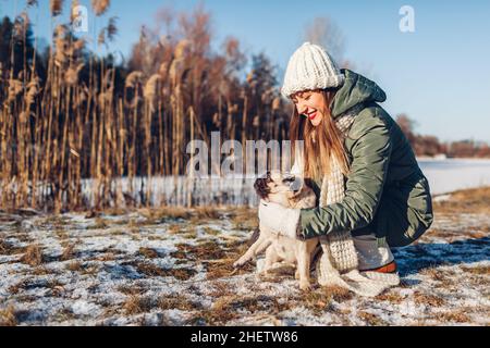 Giovane donna che cammina cane pug nel nevoso parco invernale giocando con l'animale domestico. Attività all'aperto stagionali con animali Foto Stock