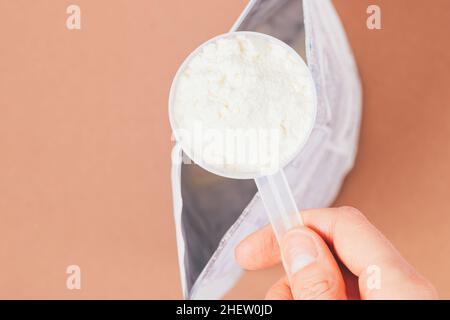 Cucchiaino dosatore con porzione di polvere proteica in confezione aperta sul tavolo marrone, vista dall'alto, primo piano Foto Stock